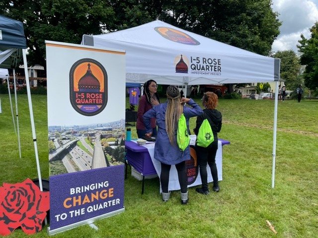 Three people in discussion, standing under the project-branded tent outside.