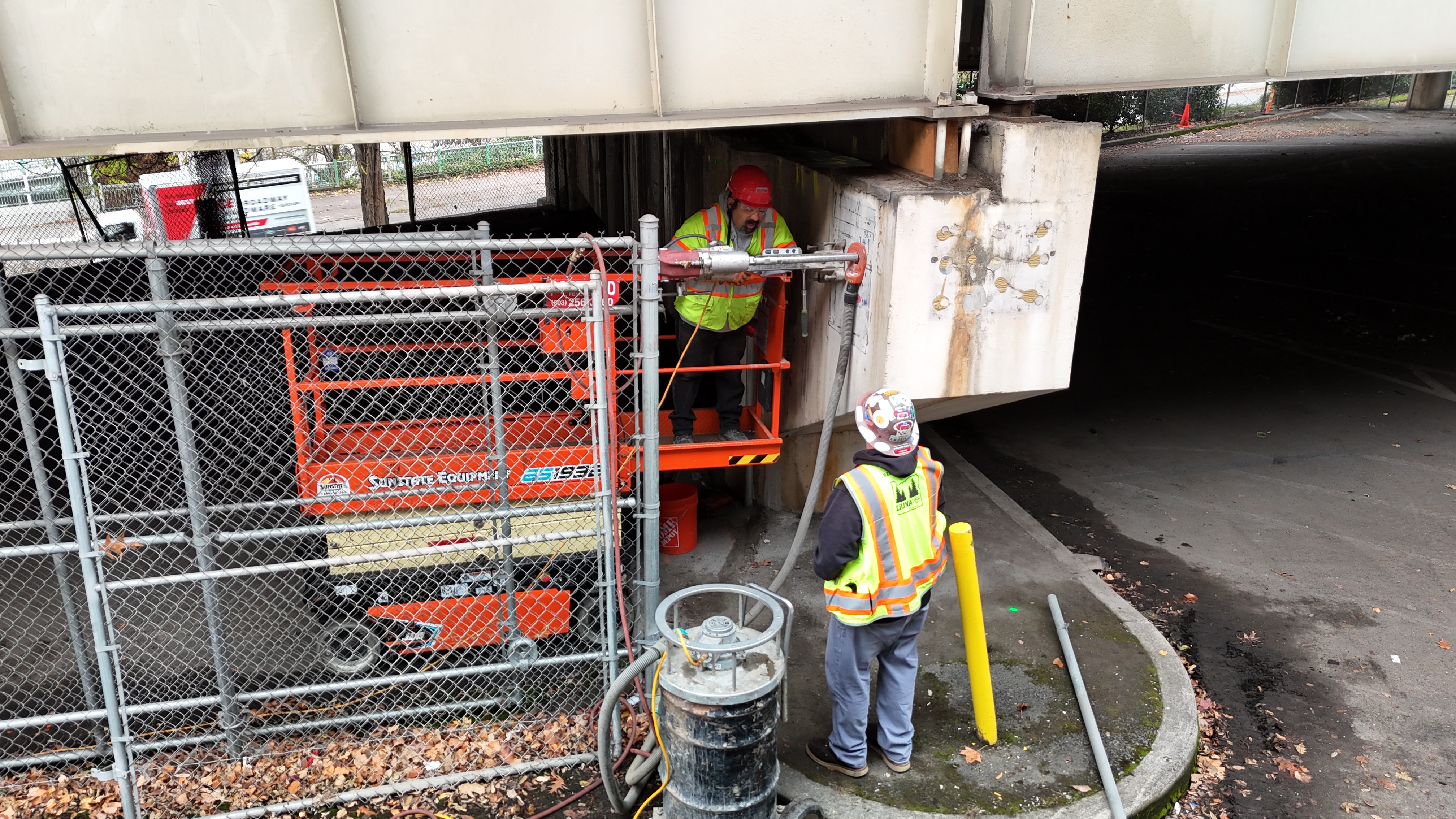Crews drill into the concrete supporting columns to install cable bolts. Lines drawn onto the cement indicate locations of rebar inside the cement.